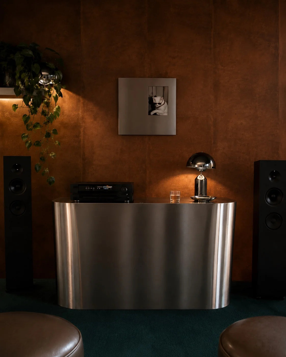 Ferrani Mono Frame on a warm brown wall above a curved steel cabinet, between speakers in a softly lit music room.
