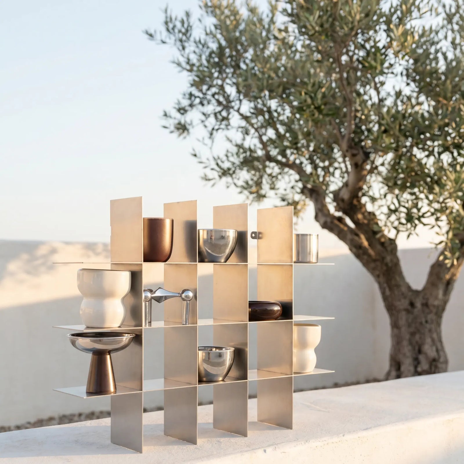 Modular metal shelf with decorative objects on a terrace beside an olive tree
